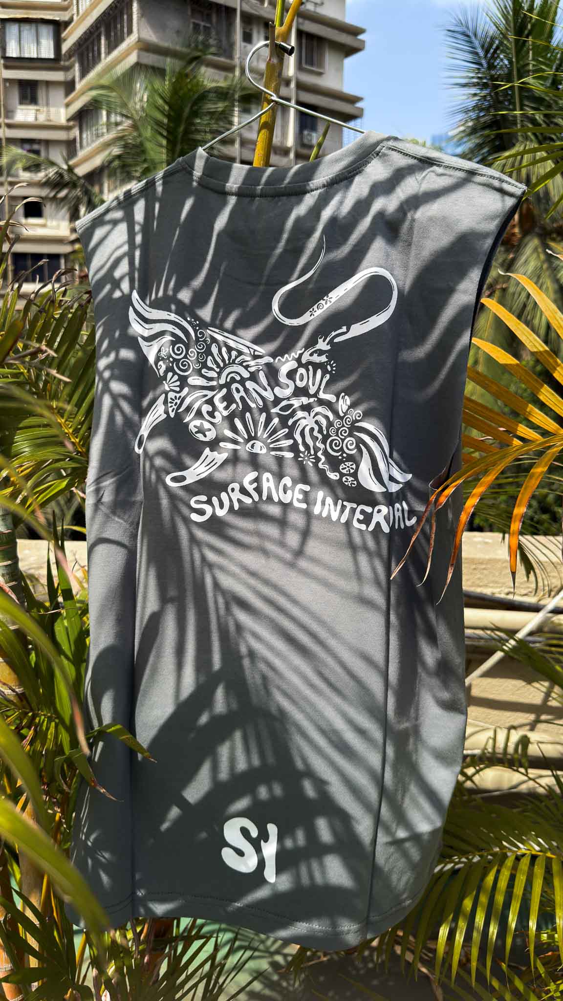 Gray sleeveless shirt with a logo and text hanging against a tropical background