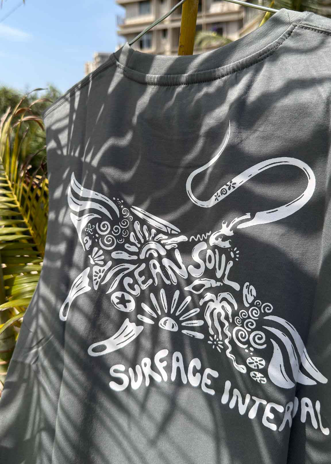 Gray t-shirt with white graphic design featuring text and a fish-like shape, hanging outdoors.