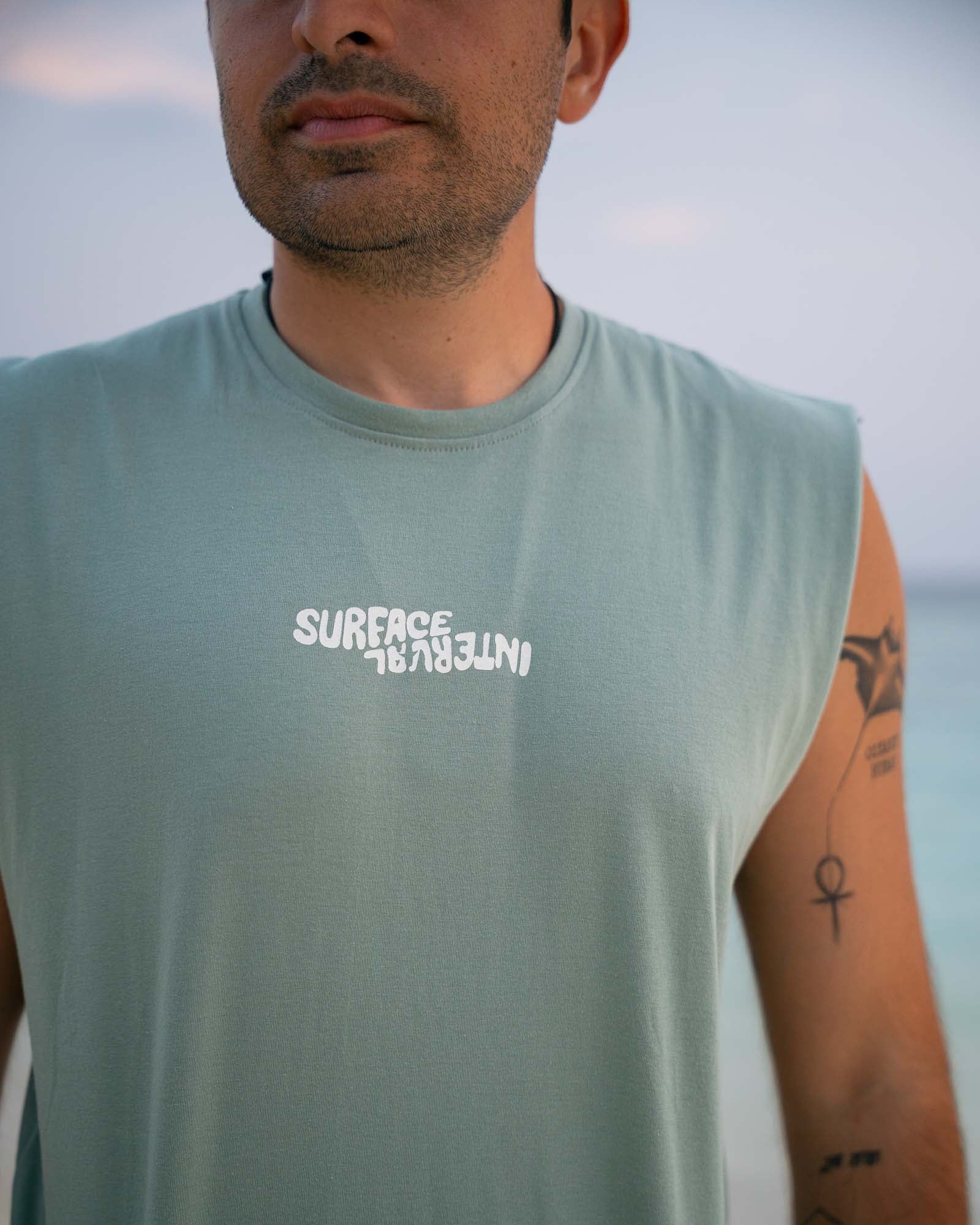 Male model wearing the Slow Living Tank Top near the ocean during golden hour