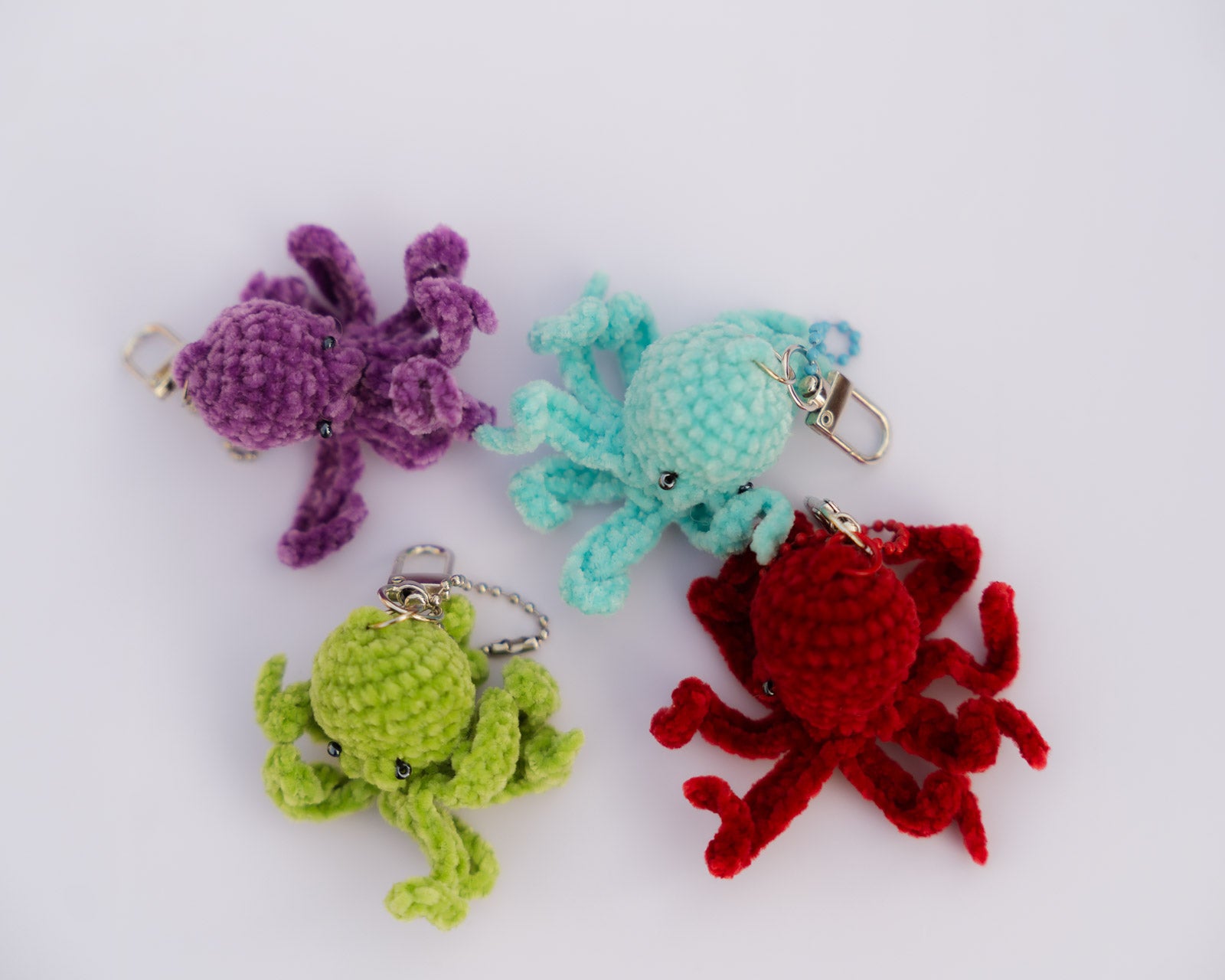 Four crocheted keychains, purple octopus, green octopus, red crab, and blue octopus made by Opi